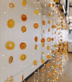 oranges are hanging from strings on the wall in front of a white wall with lights