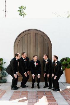 a group of men standing next to each other in front of a door wearing suits