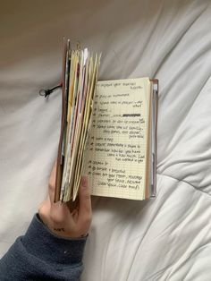 a hand holding a stack of papers in front of an open notebook on top of a bed