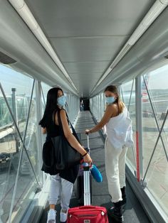 two women wearing face masks and pulling luggage