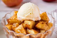 an apple dessert with ice cream in a glass bowl on a table next to apples