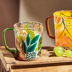 two colorful glass mugs sitting on top of a wooden table next to each other