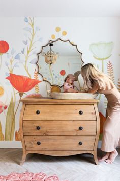 a woman standing next to a baby in a crib with flowers on the wall