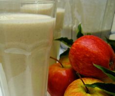 two glasses filled with milk and apples next to some other fruit on the table in front of them