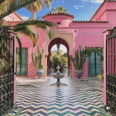 a pink building with a fountain in front of it and palm trees around the entrance