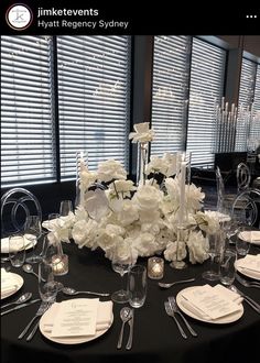 there is a table set with white flowers and place settings for dinner guests to eat