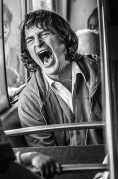 a man with his mouth wide open on a bus, yelling at someone in the mirror