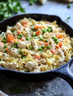 a skillet filled with chicken and noodles on top of a table next to bread