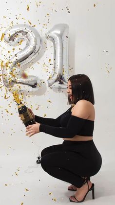 a woman kneeling down holding a champagne bottle in front of balloons and confetti