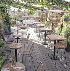 tables and chairs are set up on the wooden floored patio with potted plants