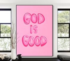 a pink painting with the words god is good on it in front of two windows