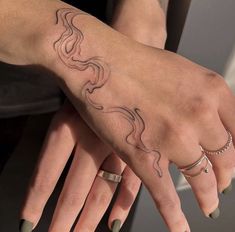 a woman's hand with tattoos and rings on her left wrist, holding onto the other