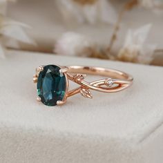 a ring with an oval blue stone surrounded by leaves and diamonds on a white surface