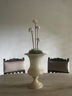 a white vase sitting on top of a wooden table next to two chairs and a bench