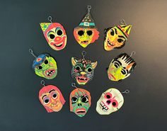 a group of different colored masks hanging from hooks on a black surface with one wearing a hat and the other wearing a cat mask