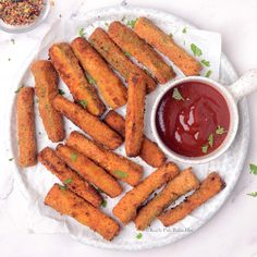 some fried food on a white plate with ketchup and dipping sauce next to it