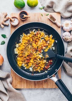 onions being cooked in a frying pan on a cutting board next to garlic and limes