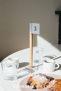 two pastries are sitting on a plate with a cup of water and a sign that says george & willy