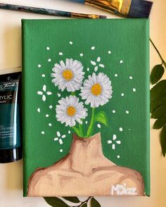 a painting of daisies in a vase on a green background next to some paintbrushes