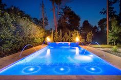 an outdoor swimming pool at night with lights on the side and water spouting out