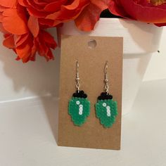 a pair of earrings with the letter i on them sitting in front of a flower