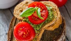 two slices of bread with tomatoes and pesto on them, sitting on top of a piece of wood