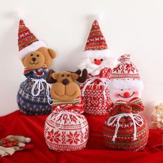 several stuffed animals in knitted christmas hats and sweaters on a red cloth covered surface