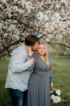 a man and woman standing in front of a flowering tree