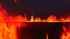 a man standing on top of a fire filled field with lots of red and orange flames