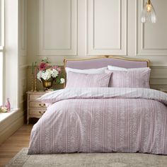 a bed with pink comforter and pillows in a bedroom next to a window,