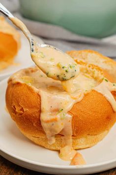 a spoon full of cheese sauce being lifted from a bread roll on a white plate