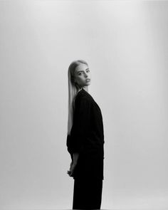 a woman with long hair is standing in front of a white wall and looking off to the side