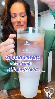 a woman holding up a glass with liquid in it and the words spooky cola 4 grape