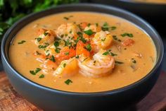 a bowl of soup with shrimp, carrots and parsley in it on a wooden board