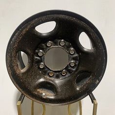 an old black wheel with holes in the center on a metal stand against a white wall