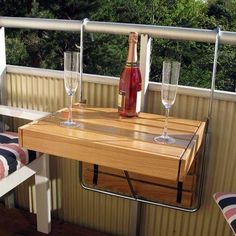 a wooden table with two wine glasses and a bottle on it sitting on a deck