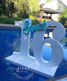 a large white sign that says sweet sixteen next to a swimming pool with trees in the background