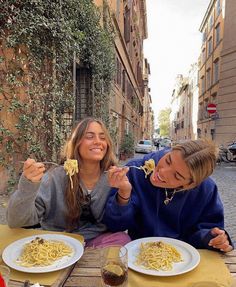 two women sitting at an outdoor table eating pasta