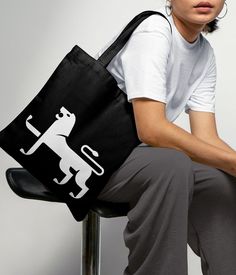 a woman sitting on a stool holding a black tote bag with a dog design