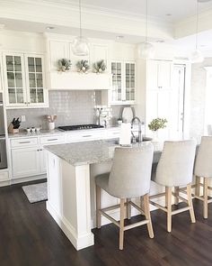 a kitchen with white cabinets and gray counter tops is pictured in this image, there are four bar stools at the center of the island