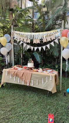 a table topped with cake and balloons in the grass