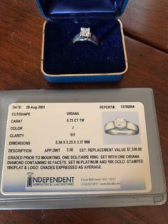 an engagement ring sits in a blue box on a wooden table next to it's receipt