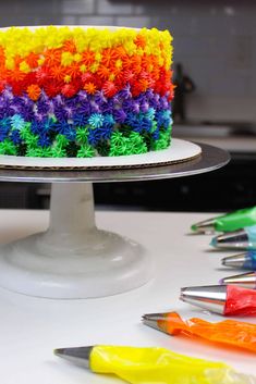 a multicolored cake sitting on top of a white table next to crayons