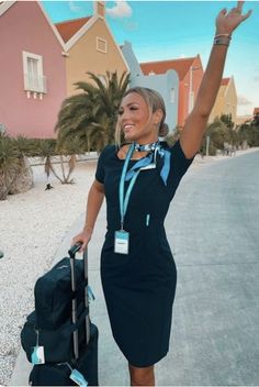 a woman in a black dress is holding her luggage and waving at the camera with both hands