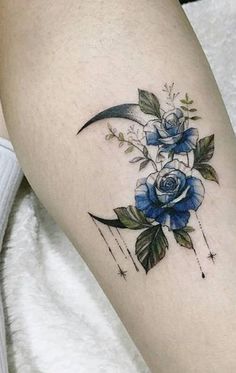 a woman's thigh with blue roses and crescent moon tattoo on it, sitting on top of a white blanket