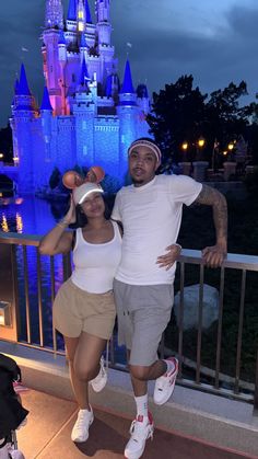 a man and woman pose for a photo in front of the disney castle at night