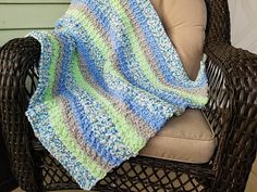 a crocheted blanket sitting on top of a chair next to a wicker chair