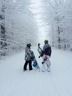 two snowboarders are standing in the middle of a snowy trail with their boards