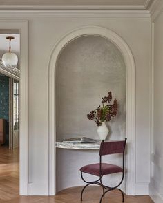 a chair sitting in front of a table with a vase on it next to a doorway