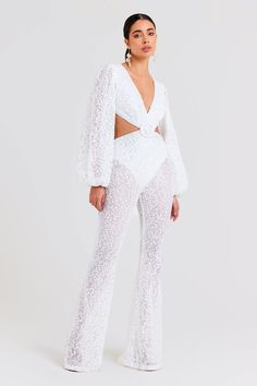 Madison White Jumpsuit Women's Clothing > Jumpsuits. DESCRIPTION & FEATURES   MADISON is a statement jumpsuit crafted from white sequin net fabric with a plunging v-neckline and gathered billowing sleeves featuring elasticated cuffs. This style includes a  cutout  to  the  back and sides, accompanied by pleat detailing at the waist band  and a round buckle belt adorned with white bead embellishments. The  bodice  of the jumpsuit is finished with a  scuba lining  and  the brief is lined in scuba Nadine Merabi, Pajama Suit, Wedding Abroad, Scuba Fabric, Net Fabric, White Jumpsuit, Buckle Belt, White Beads, Short Tops